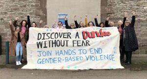 Group of women from Dundee Women's Aid with a sign saying 'Discover a Dundee without fear. Join hands to end gender-based violence.'